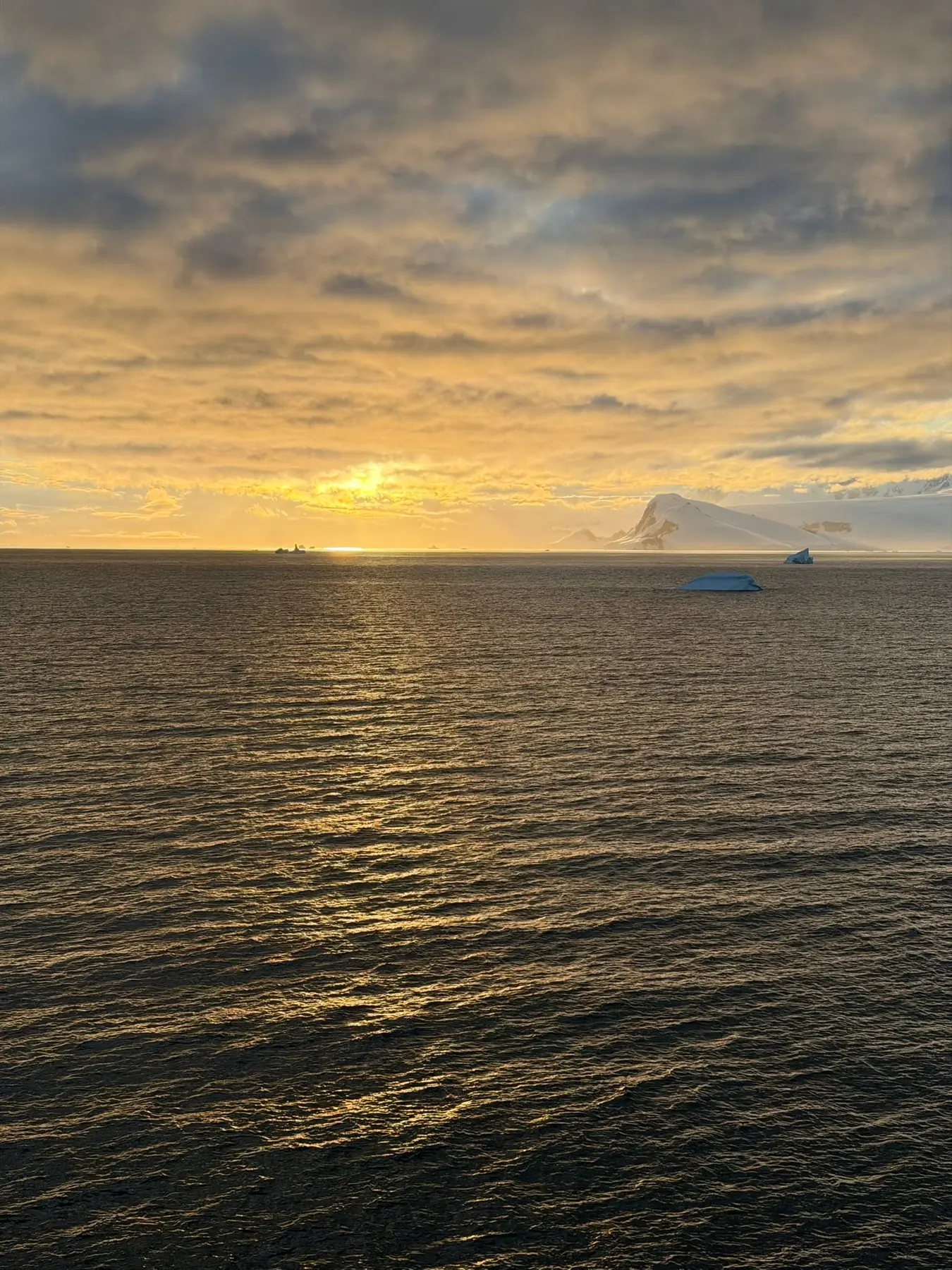 Goldener Sonnenuntergang über dem Südpolarmeer mit einem Eisberg am Horizont