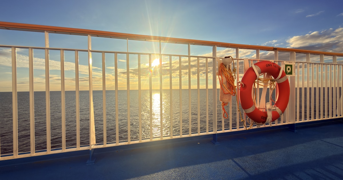 Alleinreisende Person an der Reling eines Kreuzfahrtschiffs mit Blick auf den Ozean im Abendlicht