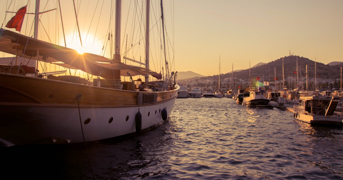 Kleine Luxus-Yacht mit Marina-Plattform vor Anker in tuerkisem Mittelmeerwasser bei Sonnenuntergang